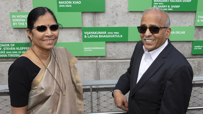 A male faculty member who is also part of the College Offices with his wife, who is wearing a gold and beige sari. They are standing in front of the FOEB.