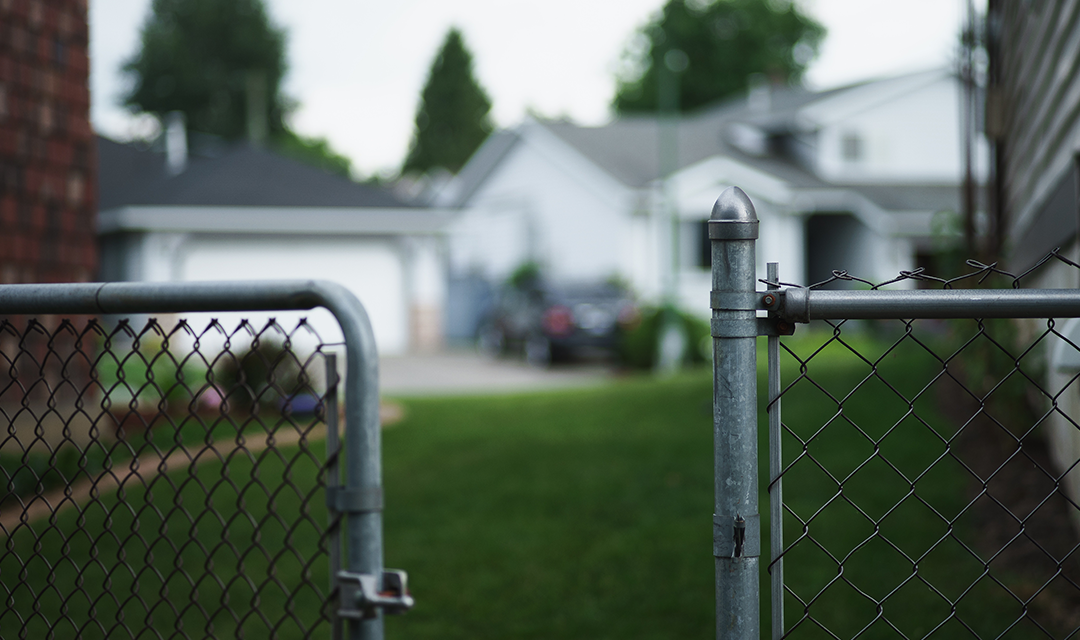 An unlocked gate in a fence surrounding a house
