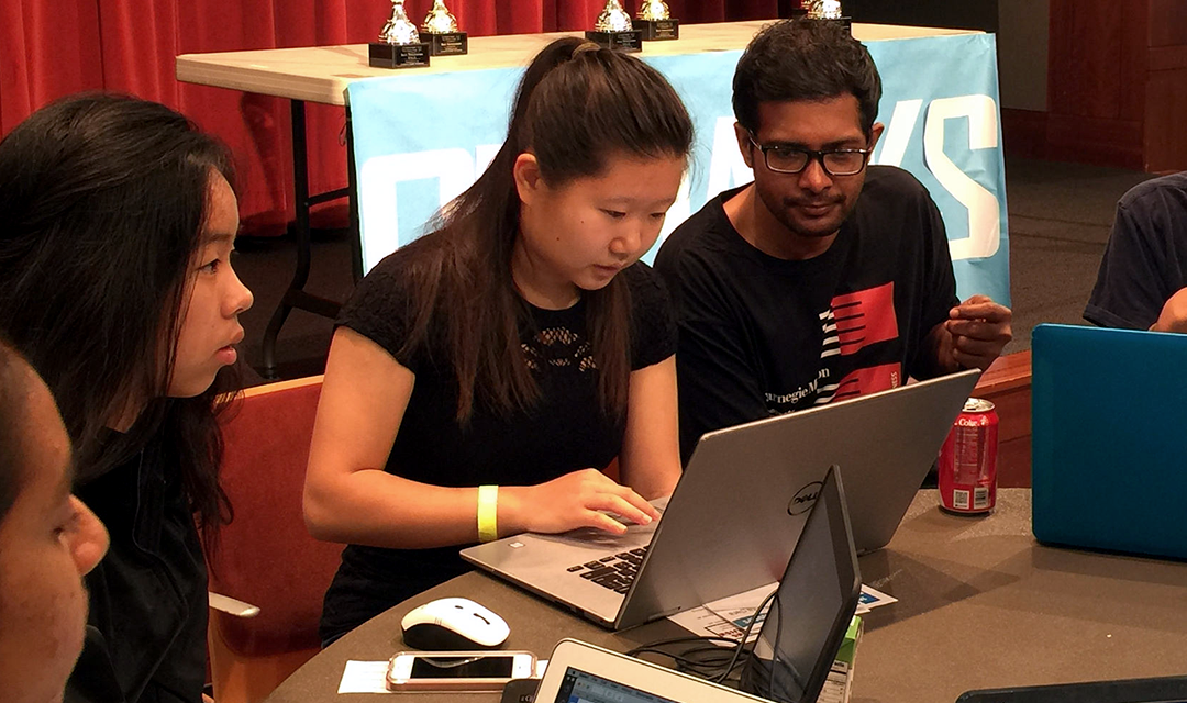 Students sit around a table and work on laptops at hackathon
