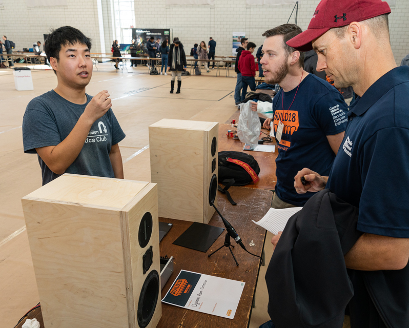 Three people around a set of wooden speakers