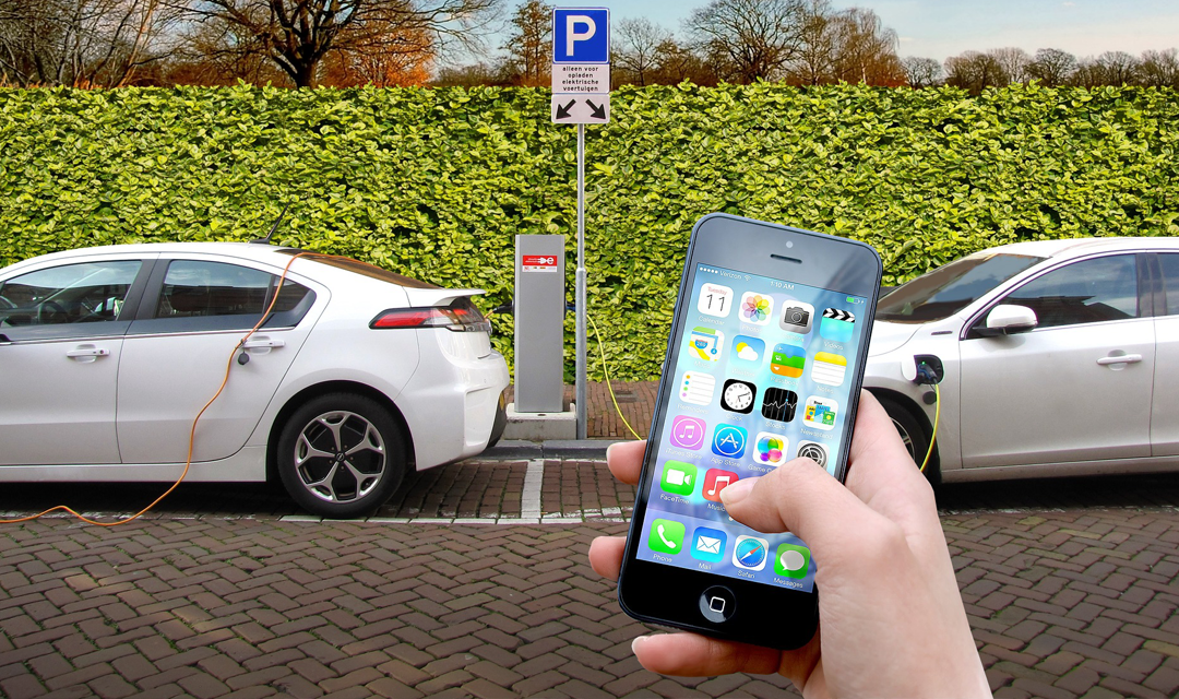 Two vehicles charging in the background with someone using a smartphone in the foreground