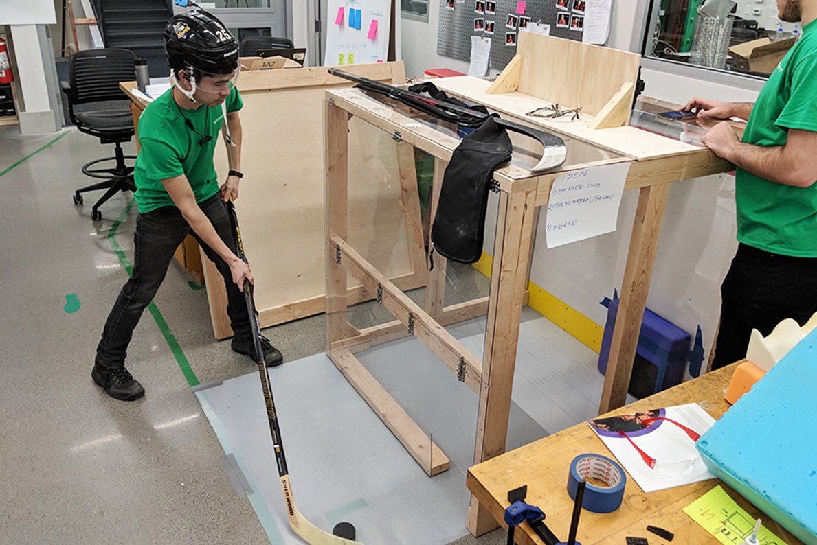 Student wearing helmet with a hockey stick and puck doing tests in a lab