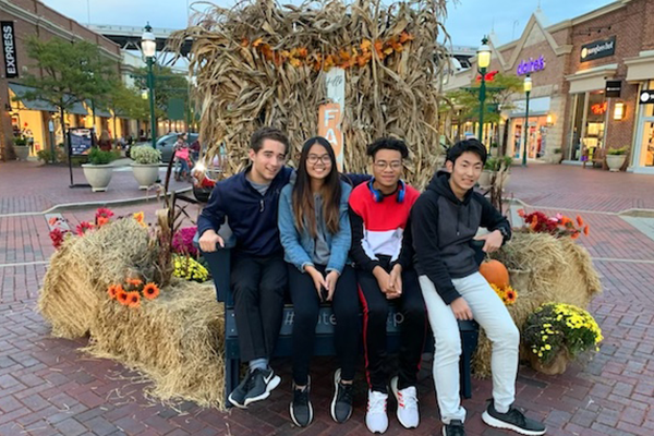 Four students outside sitting on hay bales