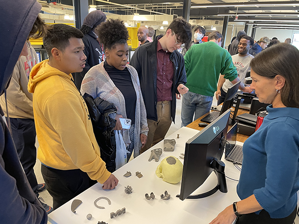 Students looking at 3d printed objects on a table while a woman talks about them