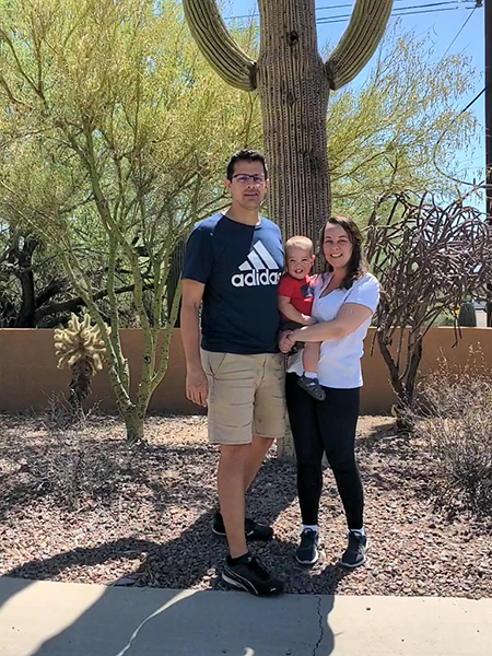 A family: husband, wife, and baby, in front of a cactus