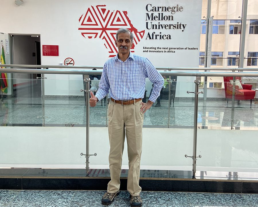 A man standing in front of the CMU-Africa logo on a wall