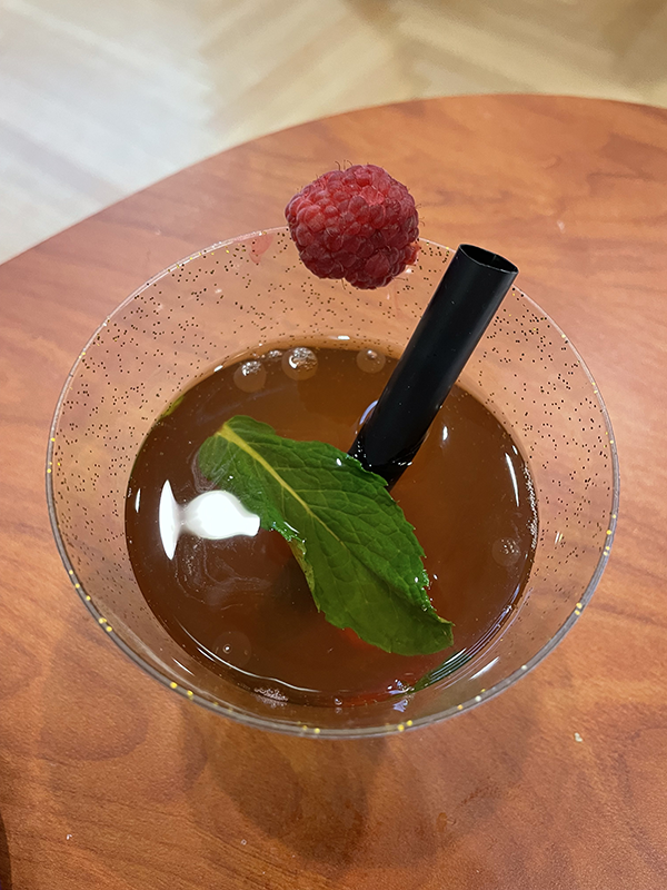 A dark beverage with a straw and raspberry on the rim