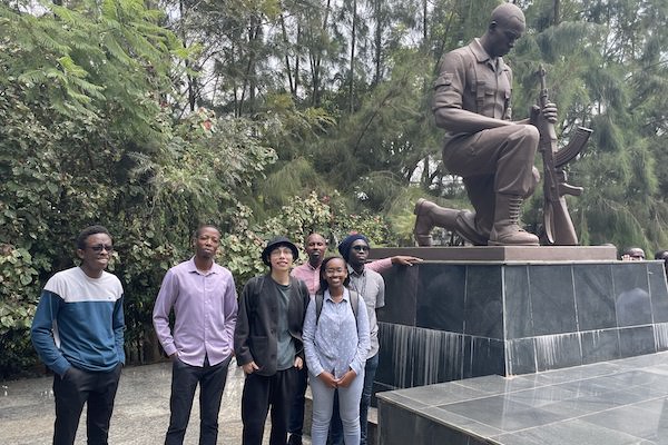 A group of students beside a statue of a kneeling man