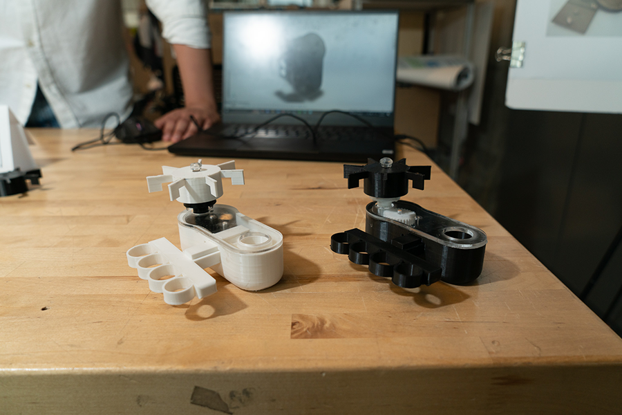 A white and a black version of the fidget toy on a lab table in front of a laptop