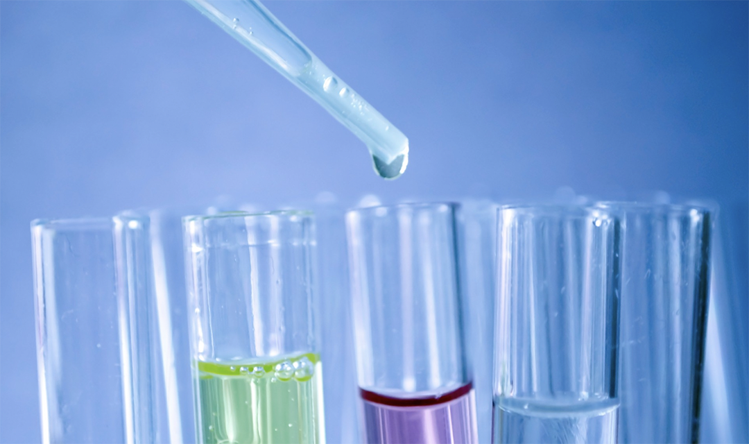 A pipette dropping liquid into multi-colored test tubes
