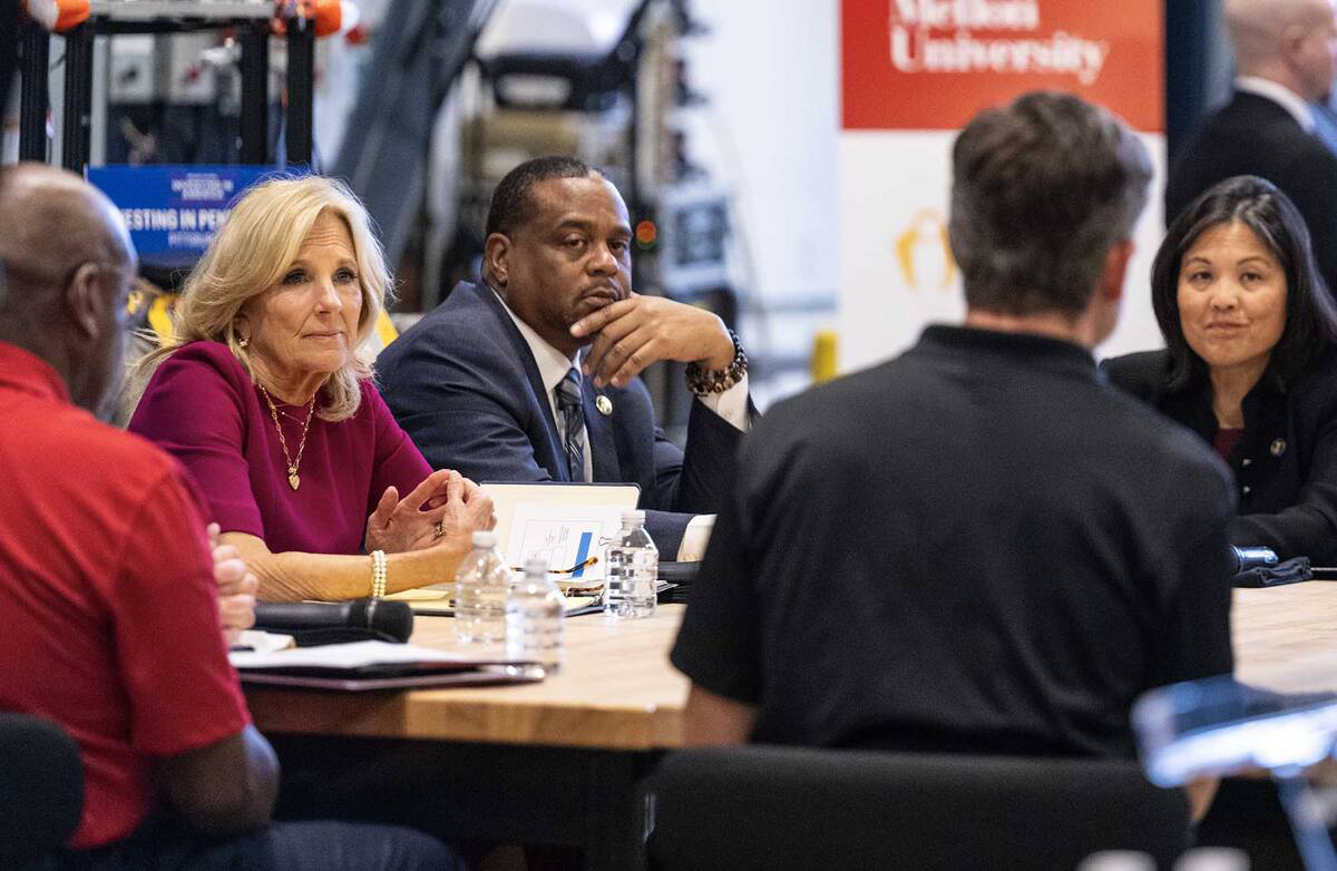 Jill Biden and Julie Su listening to a speaker at a table