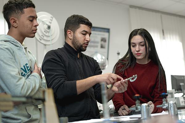 Three students in a lab, one of which is showing the others a metal tool