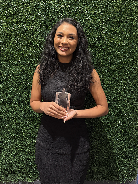 A woman holding an award in front of a ivy background.