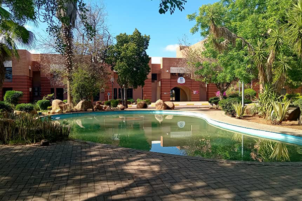 A pool outside a university building with lovely fauna surrounding it