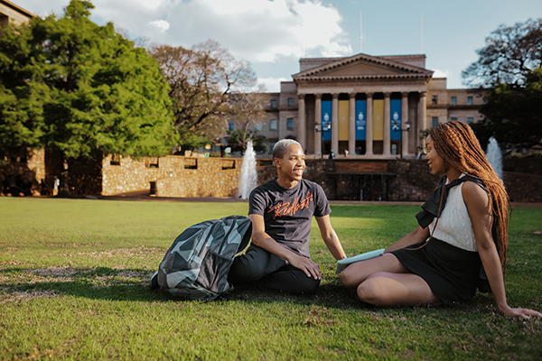 Two women sitting on grass chatting on a campus