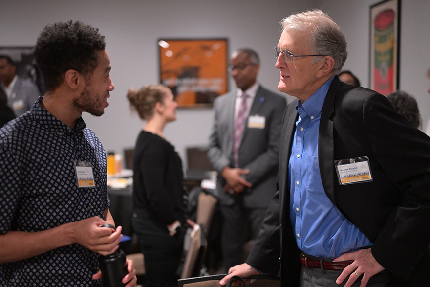 Two men speaking with other people in the background