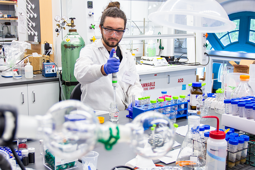A man using a pipette to put a liquid into a glass jar