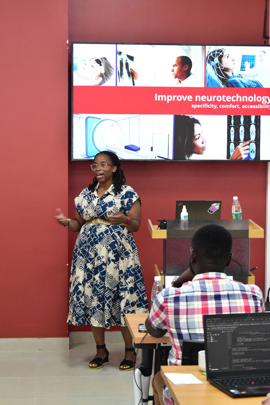 A woman in front of a group of people with a presentation behind her