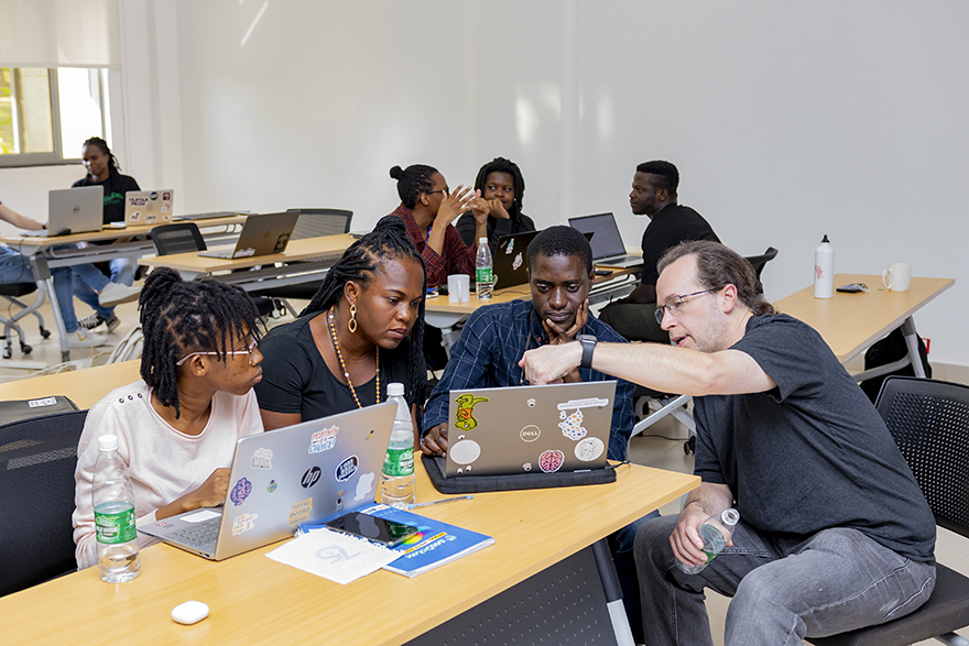 An instructor pointing at a laptop while three students listen