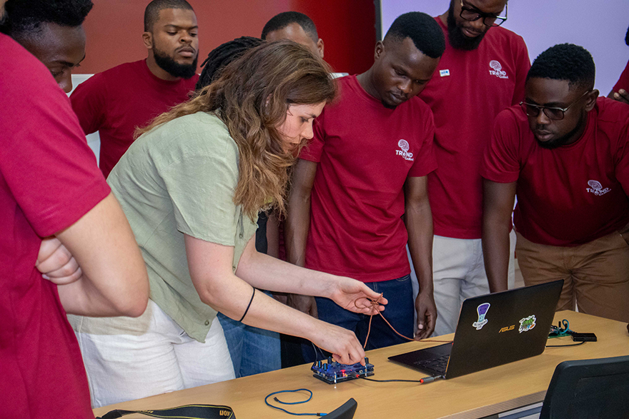 A student pushing buttons on a small electronic device that is wired into a laptop