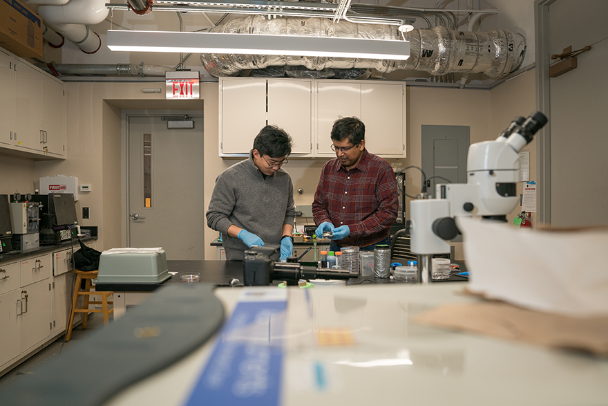 Two men holding ceramic parts and a tube in a lab