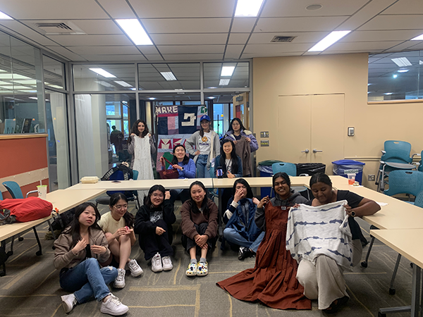 Students sitting on the floor in front of a table. One student is holding up a mending project.