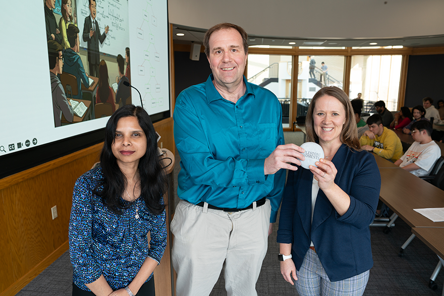 Two women stand on either side of a man who is holding up a circular object that looks like a stone