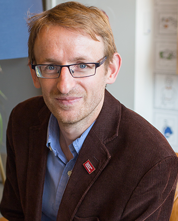 A man with glasses wearing a brown suit coat