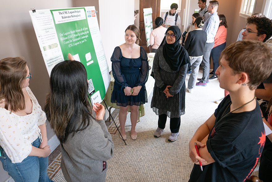 One student gestures to a project poster while four others listen