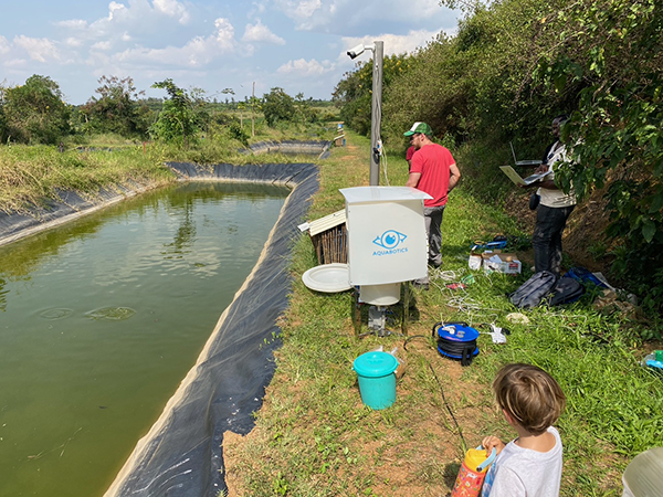 Part of a small, enclosed, rectangular pond with people and equipment on the land on the right side.