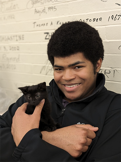 A young man holds a small black kitten.