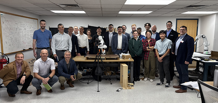 22 people in a classroom around a robotic device placed on a tripod