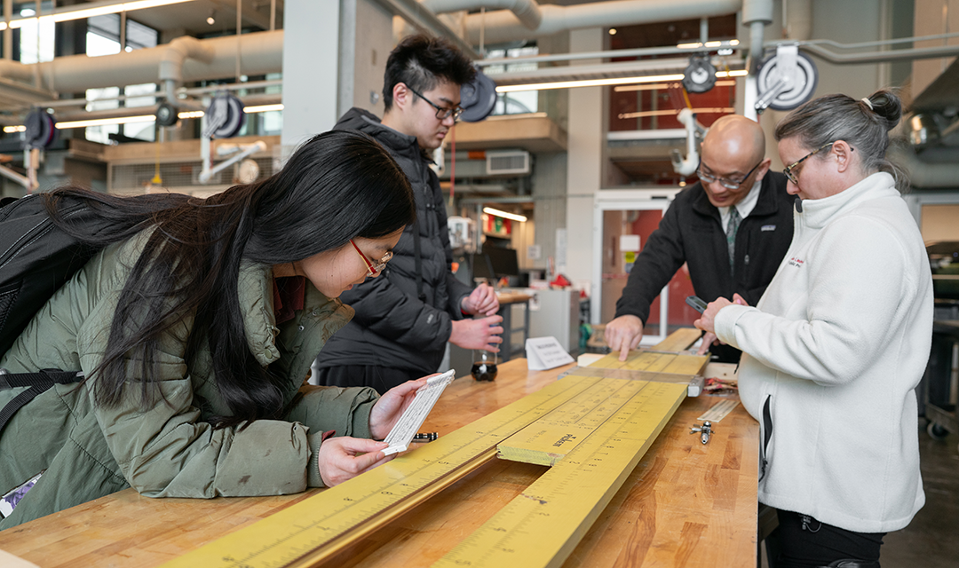 Two students and two faculty members working on a table-sized sliderule