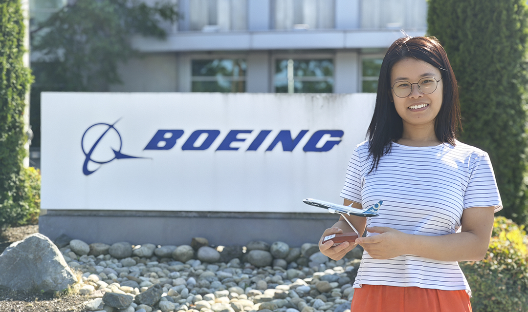 A woman holding a model plane in front of a Boeing sign