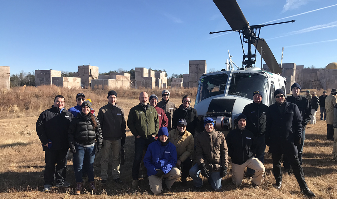 A group standing in an open field in front of a helicopter