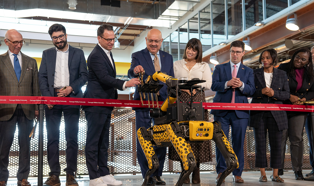 A group of people behind a red ribbon watch a robot demonstration