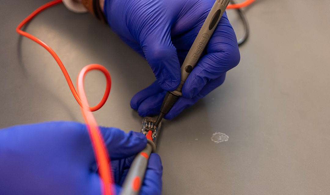 Hands working on a computer chip with two metal tools 
