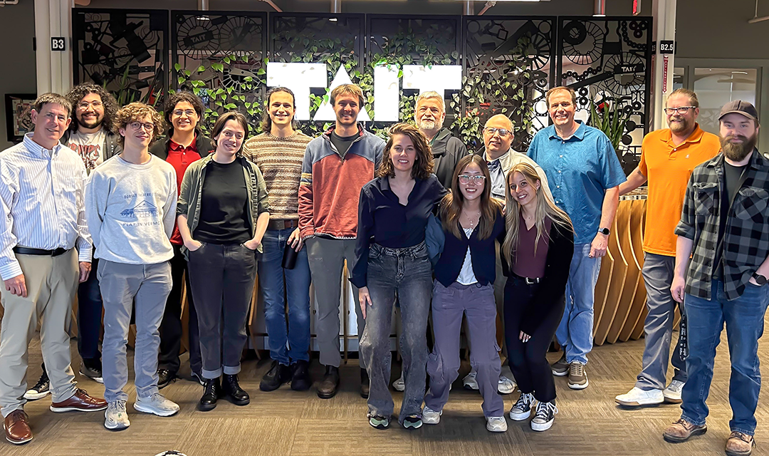 A group shot with fifteen people in front of the TAIT logo