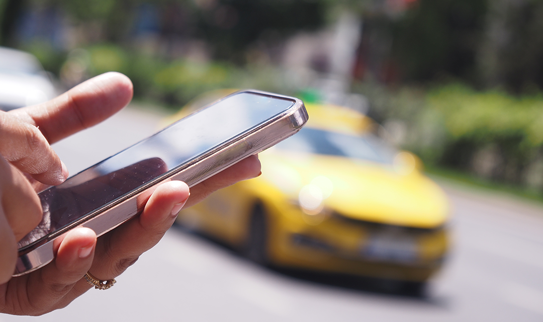 A mobile phone in someone's hand with a car in the background