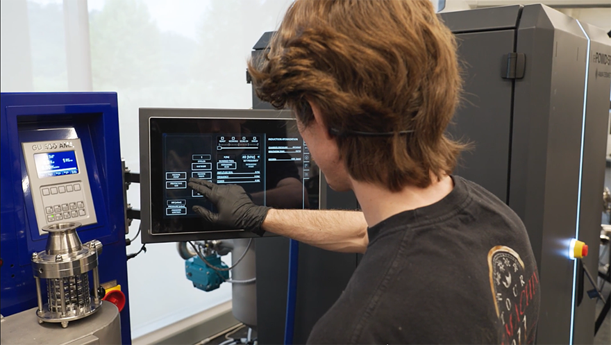 A researcher wearing black gloves operates a touchscreen control panel
