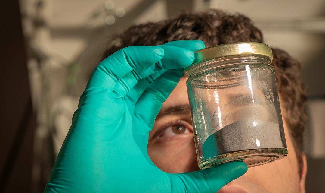 A researcher holding a jar of powder in a gloved hand