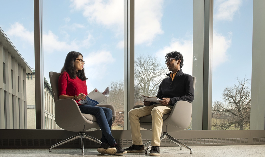 A woman and a man sit in chairs in Scott Hall, chatting and laughing together