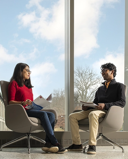 A woman and a man sit in chairs in Scott Hall, chatting and laughing together