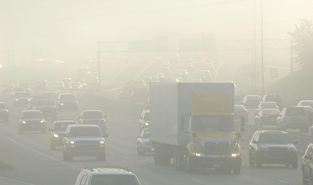 View of a busy road with cars and trucks driving in thick smog