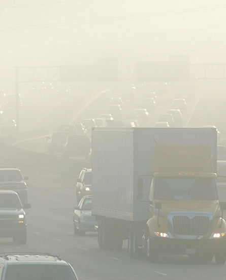 View of a busy road with cars and trucks driving in thick smog