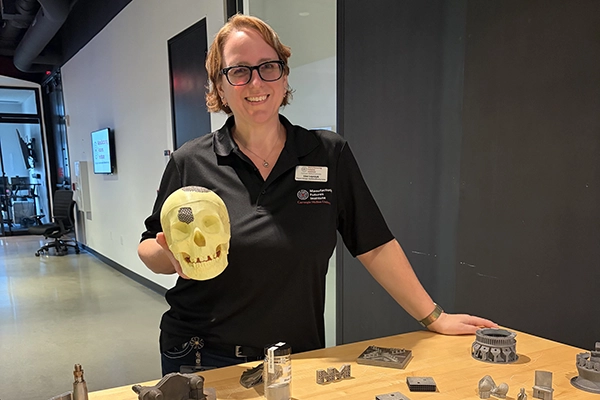 A woman holding a 3d printed skull with other printed parts on a table in front of her