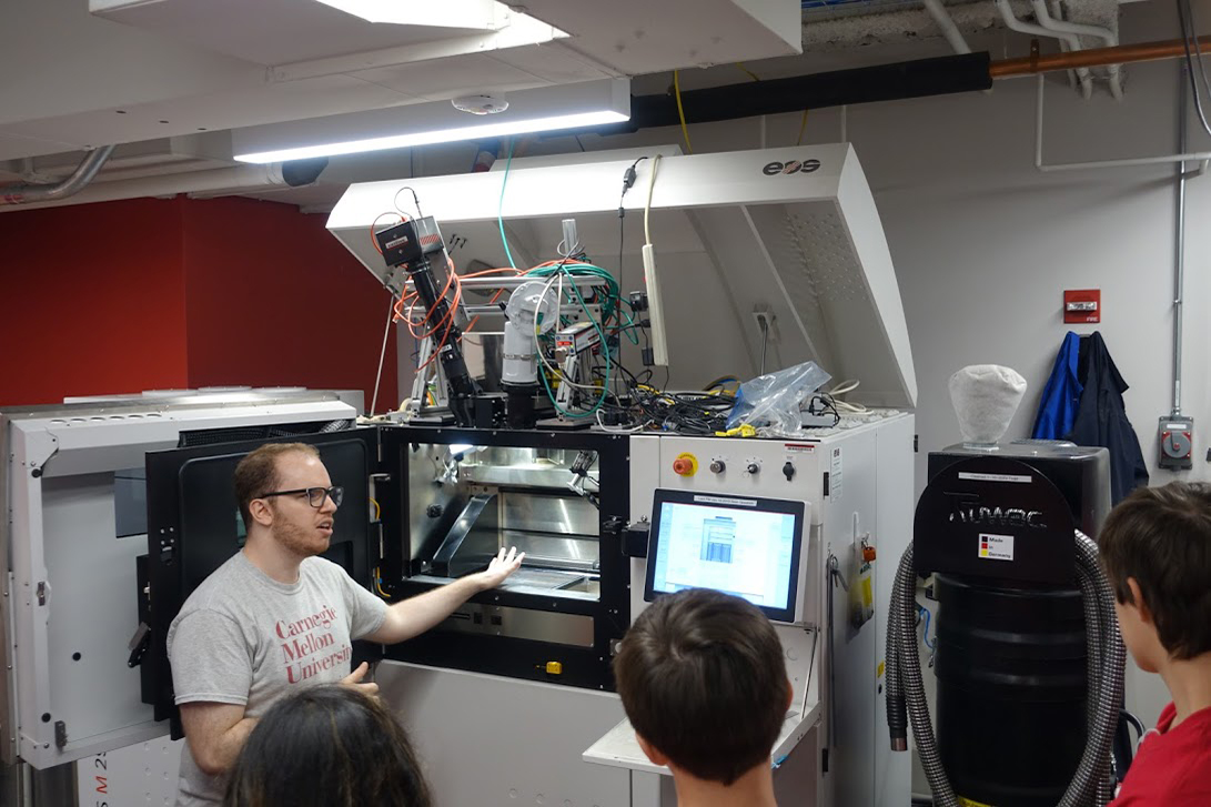A CMU student gives high schoolers a tour of the additive manufacturing lab