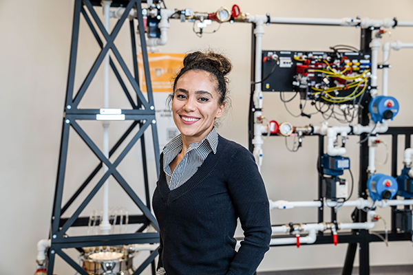 Smiling engineer standing in front of industrial piping and control equipment in a lab.